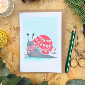 Photograph of a Risograph print greetings card with a snail character with it's shell decorated with fairy lights.